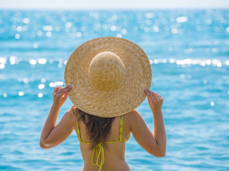 Frau steht mit Sonnenhut am Strand