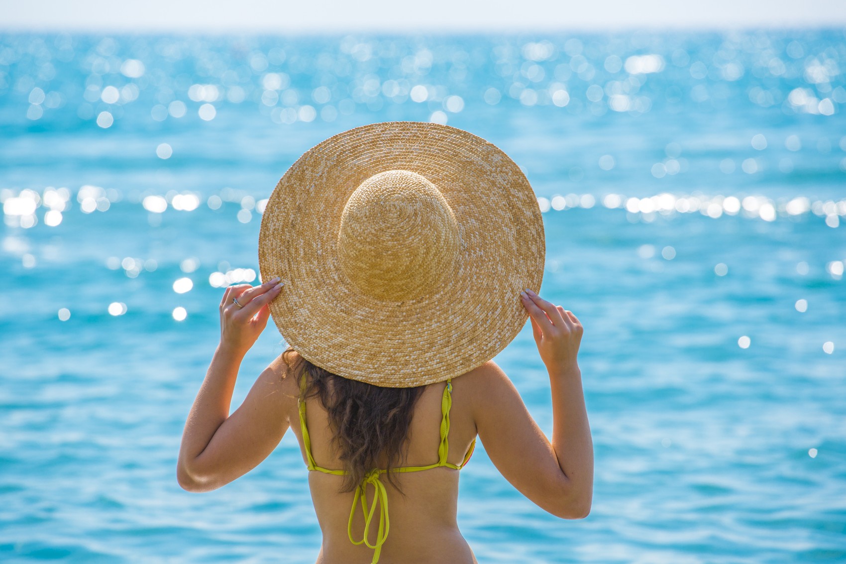 Frau steht mit Sonnenhut am Strand